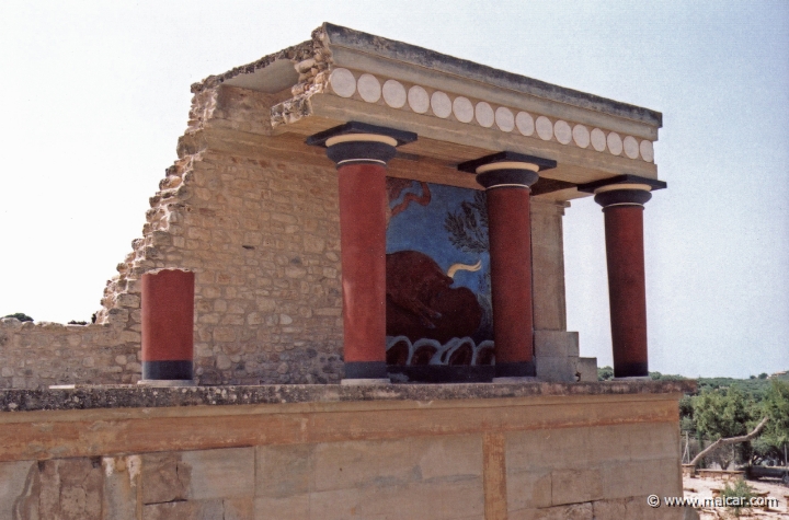 9532.jpg - 9532: Bull Bastion on the west side of the Palace of Knossos. An open air passage linked the Central Court with the North Entrance. It was paved and sharply inclined towards the north. The passage is narrow. Right and left were two raised colonnades known as “Bastions”.Arthur Evans reconstructed the “Bastion” on the west side. He also placed a copy of a restored relief fresco of a bull here. The wall painting may have formed part of a hunting scene. The passage ends in a large hall with ten square pillars and two columns. The pillars and columns probably supported a large hall on the upper floor. Evans suggested that, due to its position on the seaward side, it was here that the produce of seaborne trade would have been checked when it reached the Palace. It was therefore named the “Customs House”. Palace of Knossos (Crete).